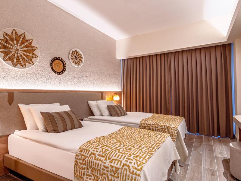 Modernes Schlafzimmer mit zwei Einzelbetten, warmem Licht, dekorativen Kissen und braunen Vorhängen.