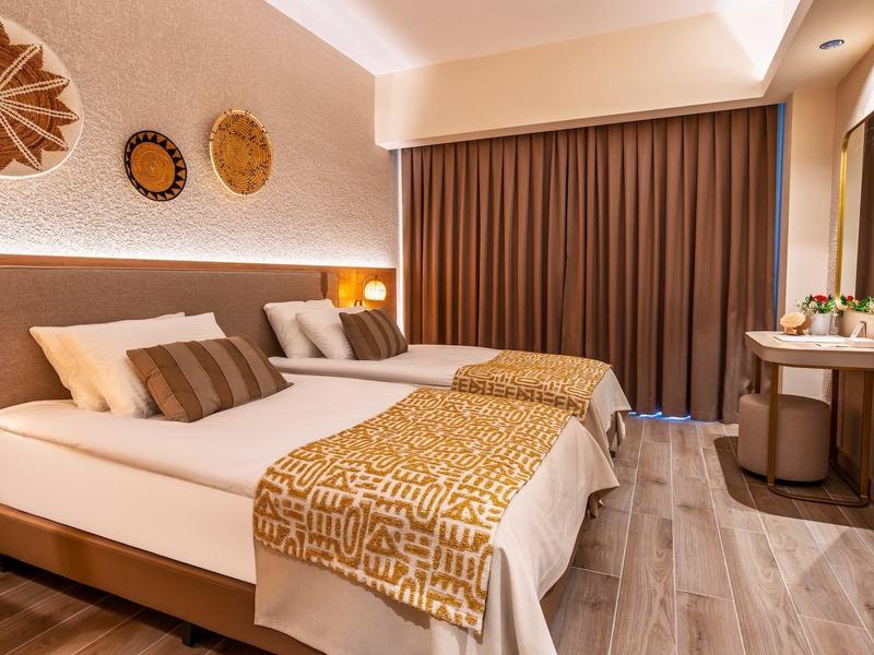 Modernes Hotelzimmer mit Doppelbett, braunem Vorhang, Holzboden und Wandfernseher.