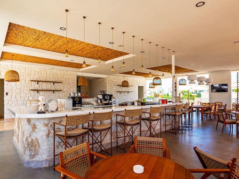 Moderner, heller Gastraum mit langer Marmorbar, Holzmöbeln und hängenden Lampen in warmen Tönen.