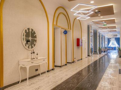 Long couloir d'hôtel avec miroir décoratif, meuble et éclairage moderne au plafond.