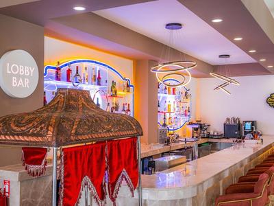 Bar d'hôtel lumineuse avec long comptoir, tabourets de bar et un auvent décoratif avec rideaux rouges.