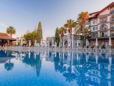 Hôtel avec grande piscine, transats et palmiers sous un ciel clair.