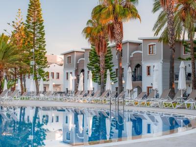 Hôtel avec piscine extérieure entourée de palmiers au coucher du soleil.