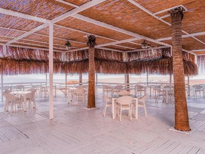 Terrasse couverte avec poutres en bois et toit de chaume, tables et chaises avec vue sur la mer.