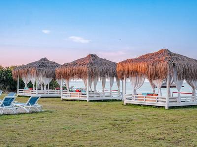 Transats sous toits de chaume sur une pelouse verte avec ciel bleu.