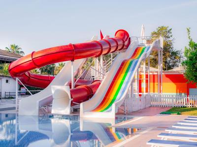 Grande glissade d'eau avec rayures colorées et toboggan tunnel rouge à côté de la piscine d'une station de vacances.