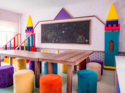 Espace enfant coloré avec table en bois, tabourets multicolores et tableau noir mural.