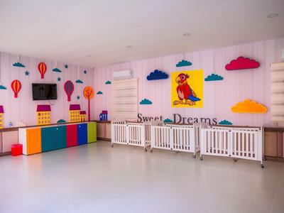 Salle de jeux pour enfants avec mobilier coloré, décorations murales de ballons et fenêtres avec grilles blanches.