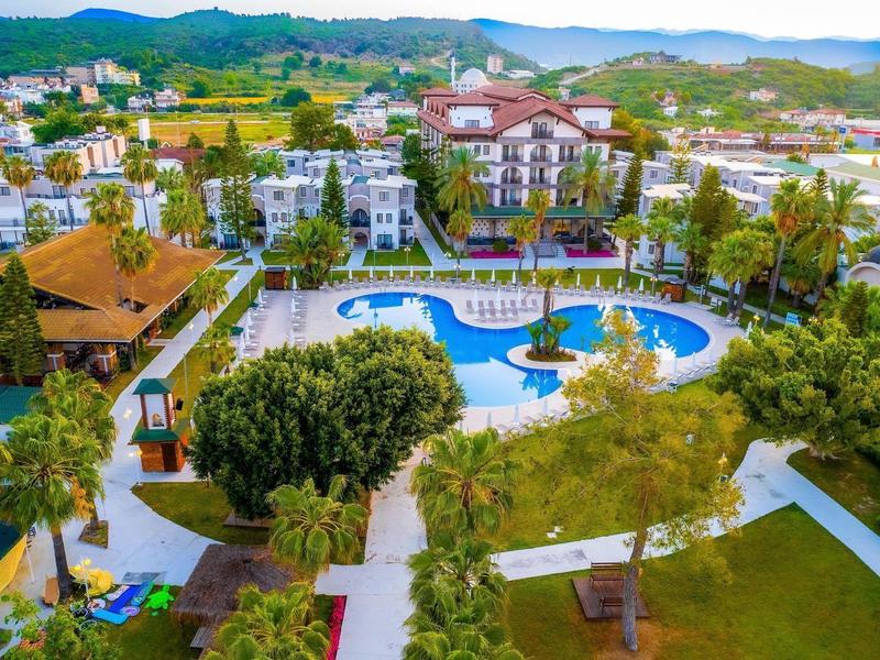 Vue aérienne d'un hôtel avec piscine, entouré d'arbres et de montagnes en arrière-plan.