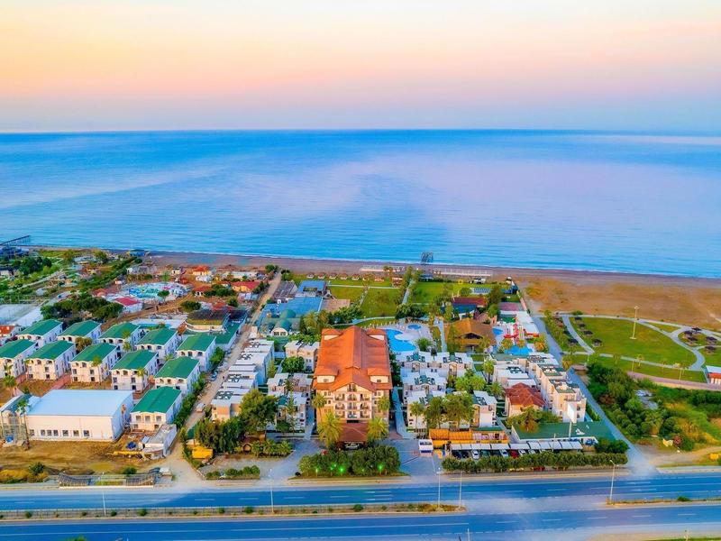 Vue aérienne d'une ville côtière avec des maisons, une route et la mer au coucher du soleil.