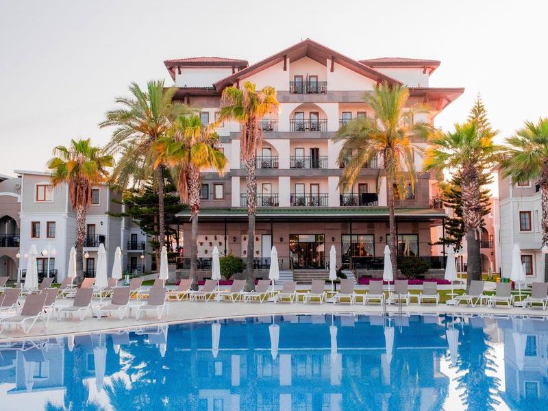 Hôtel de luxe avec palmiers et piscine dans un cadre tropical au coucher du soleil.