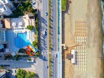 Vue aérienne d'un hôtel avec piscine à côté d'une route et d'une plage avec des transats.