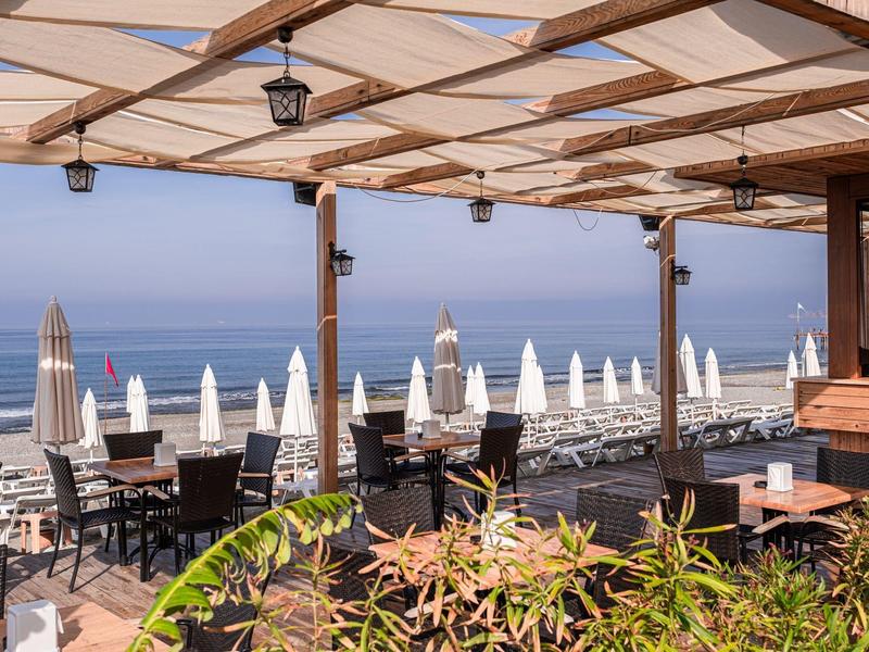 Terrasse couverte avec tables et chaises pour les clients avec vue sur la plage et la mer.