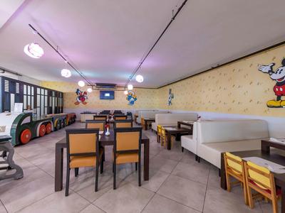 Área de juegos colorida para niños con mesas, sillas y murales en un restaurante de hotel.