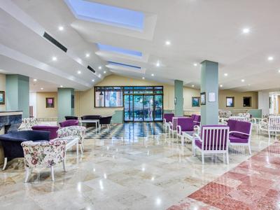 Amplia zona de vestíbulo de hotel con muchos asientos, suelos claros y ventanas en el techo.