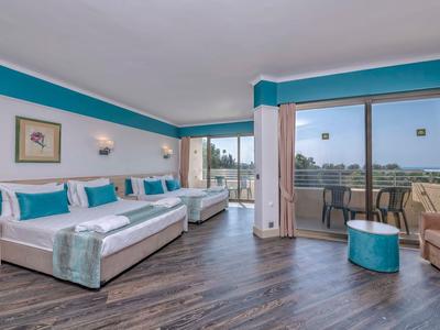 Habitación de hotel luminosa con cama doble, balcón y acentos azules, con vista al paisaje.