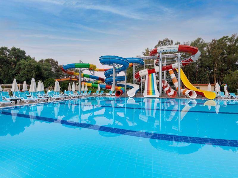 Una gran piscina con toboganes acuáticos y tumbonas bajo un cielo azul.