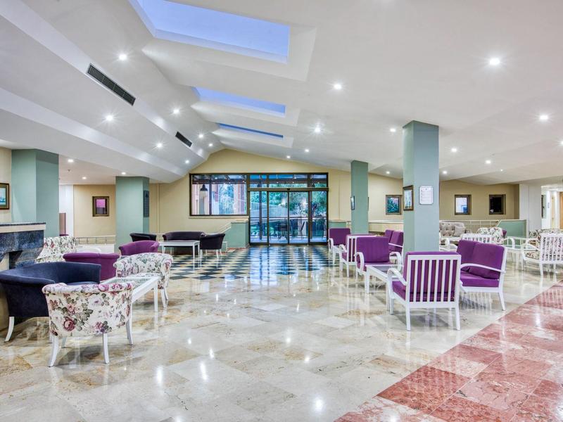 Amplia zona de vestíbulo de hotel con muchos asientos, suelos claros y ventanas en el techo.