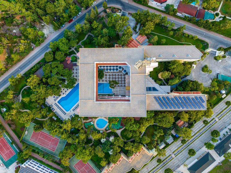 Vista aérea de un hotel con piscina, rodeado de árboles verdes y calles en un área residencial.