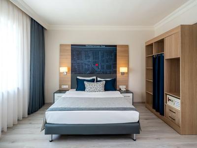 Camera d'hotel moderna con letto matrimoniale, grandi finestre e mobili in legno.