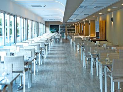 Ampia sala da pranzo vuota con sedie e tavoli bianchi, molte finestre e pavimento in legno.