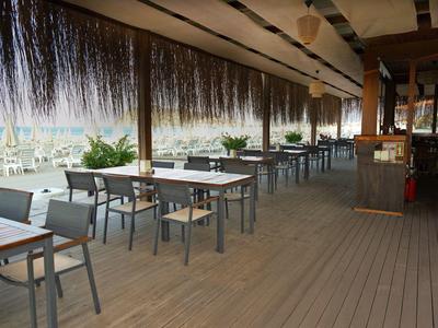 Terrazza coperta con tavoli e sedie sulla spiaggia con vista sul mare e ombrelloni.
