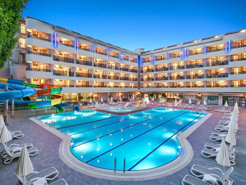 Grande hotel con piscina illuminata e lettini al crepuscolo.