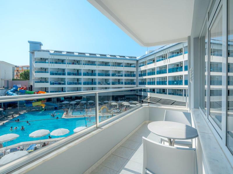 Balcone con vista su un hotel con piscina e ombrelloni in una giornata di sole.