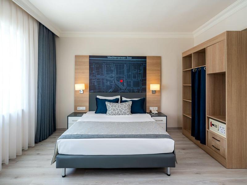 Camera d'hotel moderna con letto matrimoniale, grandi finestre e mobili in legno.