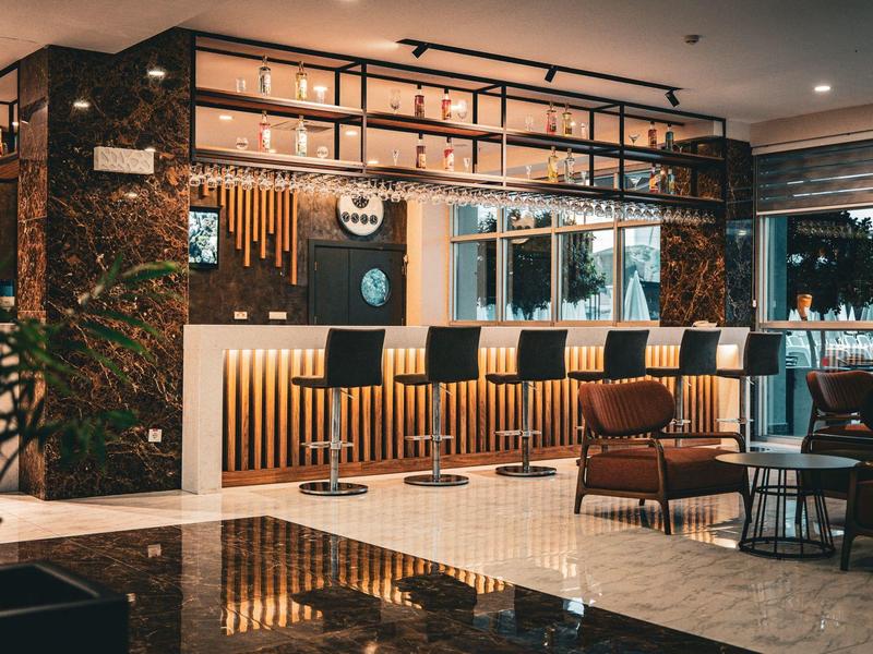 Bar dell'hotel moderno con sgabelli, rivestimenti in legno e zona salotto accogliente con luce soffusa.