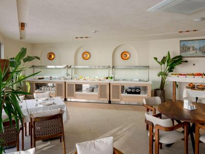 Ein heller Frühstücksraum mit Buffet, Pflanzen und gedeckten Tischen in einem Hotel.