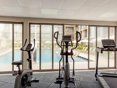 Innenraum mit Fitnessgeräten und Blick auf einen Außenpool durch große Fenster.