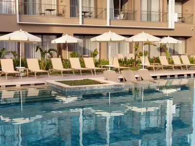 Hotelpool mit Liegestühlen und Sonnenschirmen vor einem modernen Hotelgebäude.