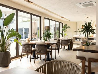 Heller Hotel-Speisesaal mit großen Fenstern, Holzstühlen und grünen Pflanzen.