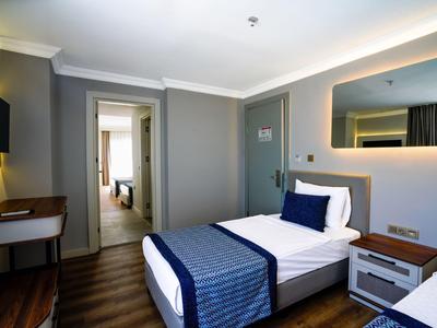 Modern eingerichtetes Hotelzimmer mit Einzelbett, Holzboden und hellgrauen Wänden.