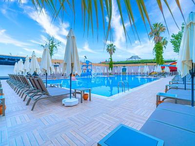 Moderner Hotelpool mit Liegestühlen und Sonnenschirmen unter Palmen im Freien.