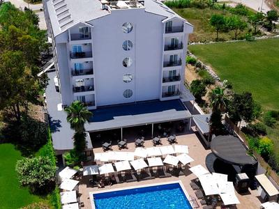 Weißes Hotel mit Pool und Liegestühlen, umgeben von grünen Wiesen und Blick aufs Meer.