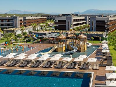 Moderní hotelový komplex s bazénem, vodním hřištěm a lehátky na slunci.