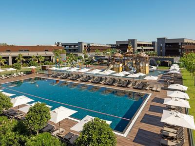 Velký hotelový bazén s lehátky a slunečníky v upravené zahradě.