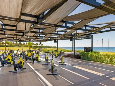 Outdoor-Fitnessbereich mit Spinning-Fahrrädern und Blick aufs Meer bei Sonnenschein.
