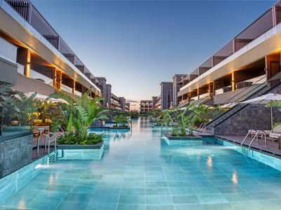 Moderner Hotelpool mit beleuchteten Wasserflächen und üppiger tropischer Vegetation.