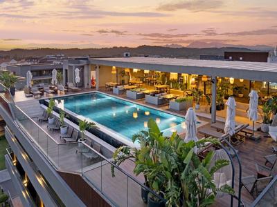 Střešní terasa s osvětleným bazénem a posezením při západu slunce.