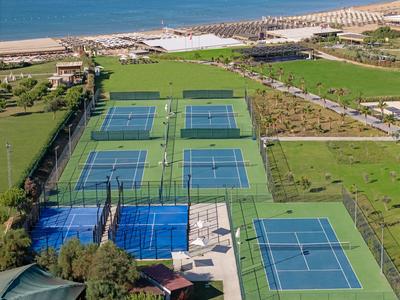 Mehrere Tennisplätze zwischen grünen Rasenflächen mit Strand und Meer im Hintergrund.