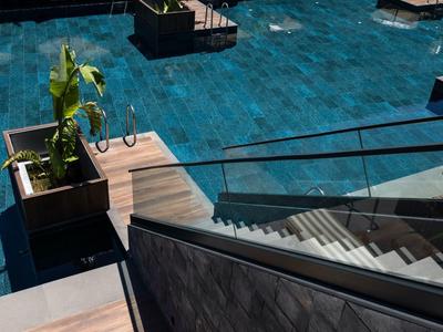 Moderní venkovní prostor s modrými vodními plochami a schody se skleněným zábradlím.