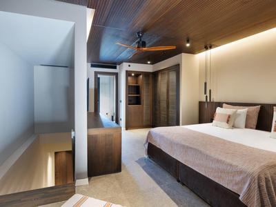 Moderní hotelový pokoj s velkou postelí, stropním ventilátorem a teplým dřevěným dekor.