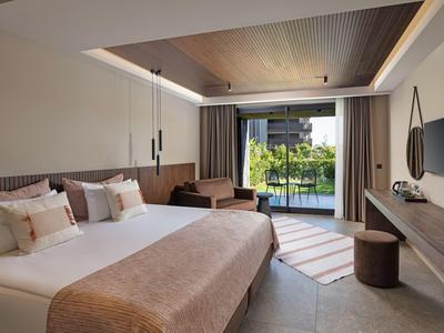 Moderně zařízený hotelový pokoj s velkou postelí a výhledem na terasu a zahradu.