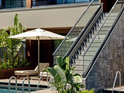 Moderní hotelový bazén se slunečníkem, lehátky a schody do patra.