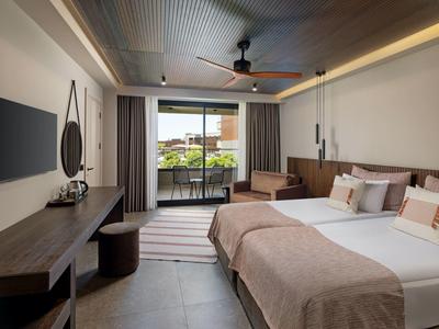 Moderní hotelový pokoj s manželskou postelí, televizí, psacím stolem a balkonem s výhledem.