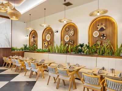 Moderní restaurace s dřevěnými židlemi, rostlinami a dekorativními oblouky na stěnách.