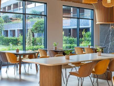 Moderní jídelna s velkým stolem, židlemi a výhledem na zahradu a budovu.